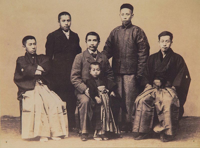 ميناكاتا كوماغوسو (يقف على يسار الصف الثاني) وعائلته في صورة ملتقطة عام 1901، وفيها أيضا سون يات-سين (يجلس على يمين كوماغوسو) وكان قد التقى كوماغوسو عندما كان يعيش في لندن. الأشخاص الآخرون هم (من اليسار إلى اليمين)، تسونيغوسو الأخ الأصغر لكوماغوسو، وتسونيتارو ابن تسونيغوسو، والمترجم الصيني وين بينغتشين، وكوسوجيرو وهو أخ أصغر آخر لكوماغوسو.