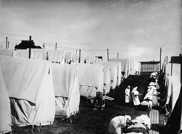 1918年のインフルエンザ流行中、簡易ベッドや屋外テントに横たわるインフルエンザ患者を治療する覆面をした医師と看護師(Photo by Hulton Archive/Getty Images)