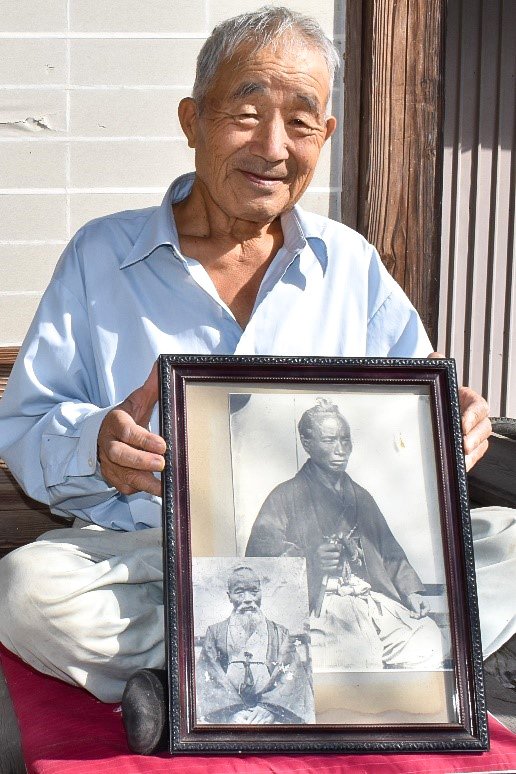 佐久間庸軒の写真(右は若かりし頃、左は晩年)の入った額を手にする4代目の子孫にあたる佐久間求さん(筆者撮影)