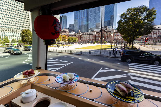 東京駅をはじめ名所を背景にすしが流れる