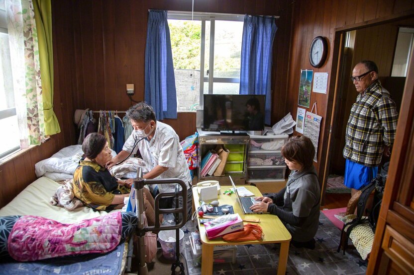 伊佐ツルさん(95)を診るドクターゴン。月に1〜2回、ドクターゴン診療所の医師が訪問している。照雄さんが(右)が心配そうに見守っていた