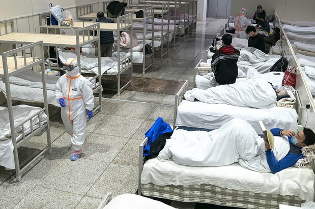 Медицинский работник в защитном костюме проходит мимо пациентов с коронавирусом, которые проходят лечение во временной больнице, расположенной в выставочном центре в Ухане, провинция Хубэй, 5 февраля 2020 г. (© Chinatopix / AP / Aflo)