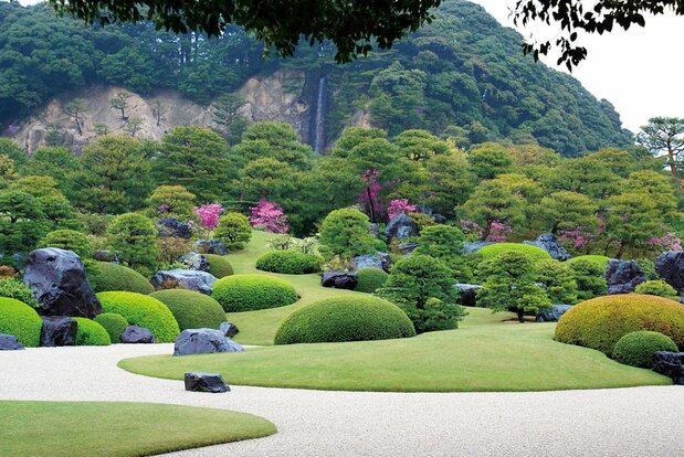 足立美術館の「枯山水庭」の奥に見える亀鶴山には、横山大観の作品「那智乃瀧」をイメージして開瀑した高さ約15メートルの「亀鶴の滝」が流れる。（足立美術館提供、画像の転載・コピー禁止）