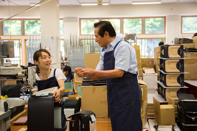 ミシン掛け最終工程担当の職人歴5年の社員に説明する土屋さん。