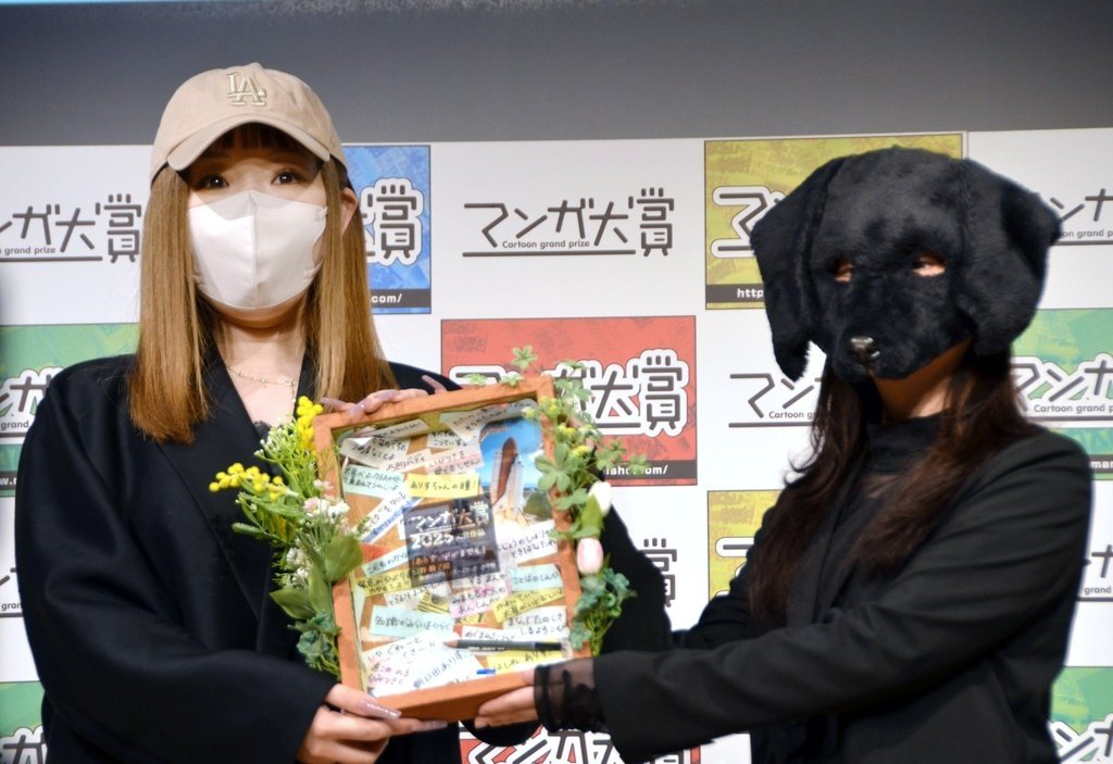 La autora de Arisu, doko made mo, Urino Kiko, recibe un premio de la ganadora del año pasado, Doronoda Inuhiko (derecha), tras ganar el Manga Taishō 2025, un galardón elegido por los libreros. (Kyōdō)
