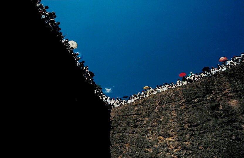 ティムカット(キリスト洗礼の日の祭り)の日、凝灰岩をくりぬいた岩窟教会を取り巻く岩壁に群がり、司祭の説教に聞き入るエチオピア正教会の信徒たち。エチオピア正教は、古代ユダヤ教の流れをくむ、エチオピアで独自に発展したキリスト教。エチオピアのラリベラで1981年撮影。『バハル アフリカが流れる』より