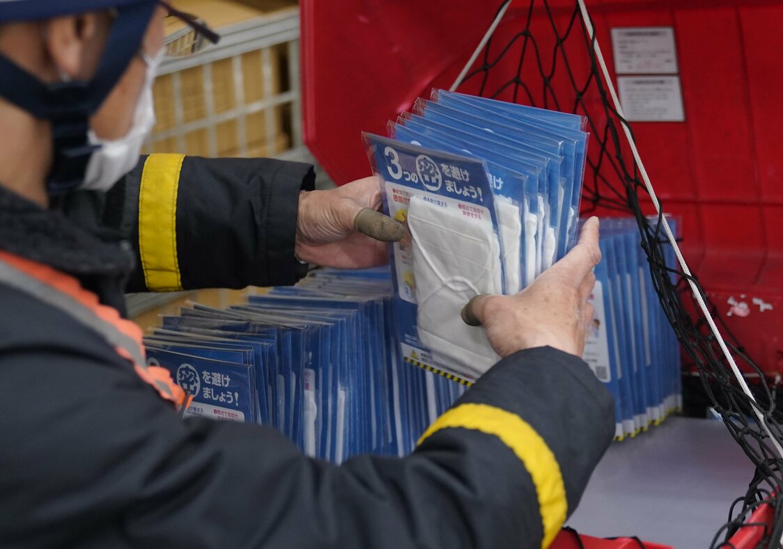 Un empleado del servicio postal ordena sobre una motocicleta de reparto varias de las mascarillas que serán enviadas a los hogares japoneses. En Setagaya, Tokio, el 17 de abril. (© Jiji)