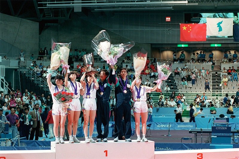 1991年世界卓球・女子団体決勝で中国を下し、南北朝鮮統一チームが優勝。青い朝鮮半島を描いた統一旗がセンターポールに上がる。（千葉・幕張メッセ）（時事）