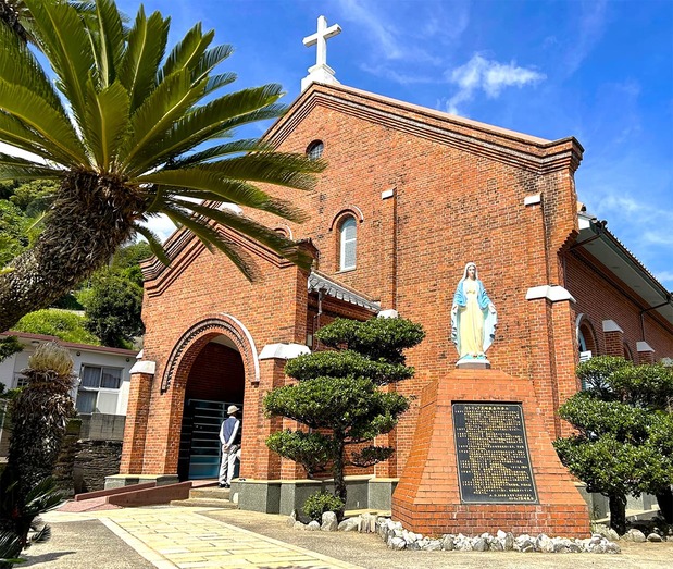 A statue of the Virgin Mary with arms held out welcomes visitors to the red brick Kurosaki Church, completed in 1920. It stands next to the Kurosaki Kyōkai-mae bus stop. (© Amano Hisaki)