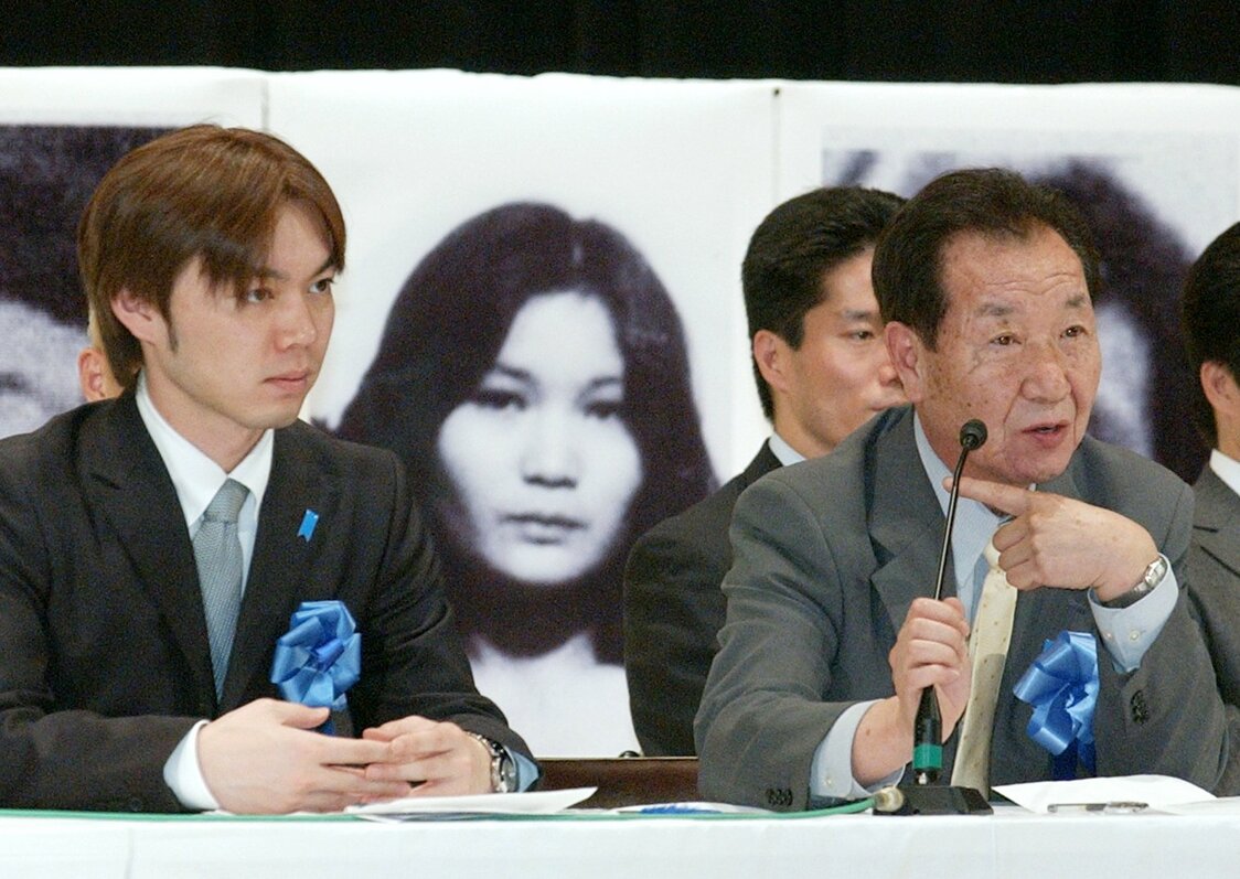 飯塚耕一郎さん（左）は母親の田口八重子さんが拉致された後、八重子さんの兄の繁雄さん（右）の子として育てられた。後方は田口八重子さんの写真（2005年4月撮影、時事）