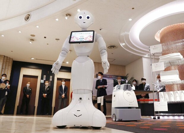 無症状や軽症の新型コロナウイルス感染者を受け入れる宿泊施設で、出迎える人型ロボット「ペッパー」。右奥はAI（人工知能）を活用した清掃用ロボット＝2020年4月30日、東京都八王子市（共同）