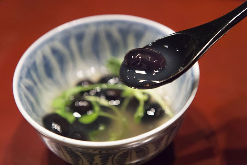 Judías negras cocidas en salsa de soja con azúcar, acompañadas con brotes de zarcillos de guisantes y regadas con pasta de judías cocidas de Yoshino-kuzu.