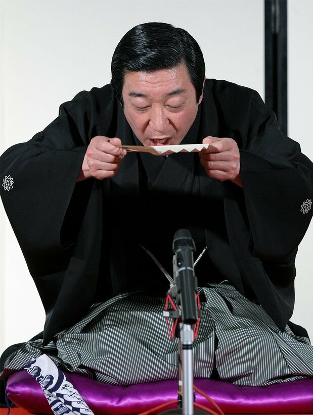 يستخدم سانيوتيي هوراكو مؤدي فن راكوغو مروحة سينسو وكأنها وعاء يحتوي ساكي يشرب منه بينما يروي إحدى قصصه. الصورة ملتقطة في مسرح أساكوسا تويوكان في طوكيو (© جيجي برس).