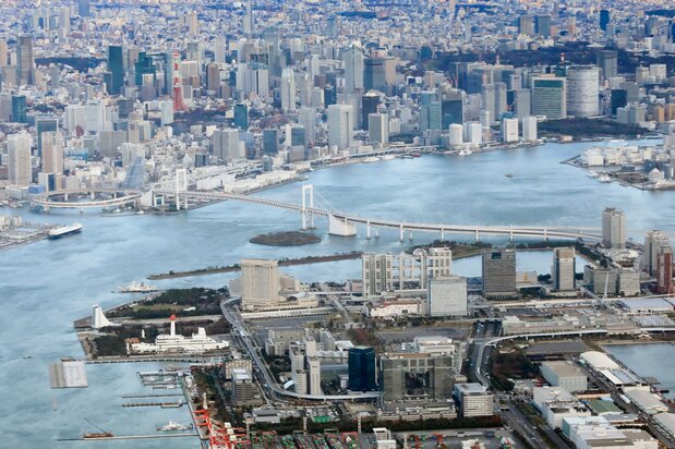 上空から見下ろした東京湾と都心部の街並み。中央左に浮かぶ緑の島が品川第六台場跡で、その右手、レインボーブリッジとフジテレビの間に見えるのが第三台場跡の台場公園。右斜め上の岸壁沿いの緑地が浜離宮恩賜公園(時事)