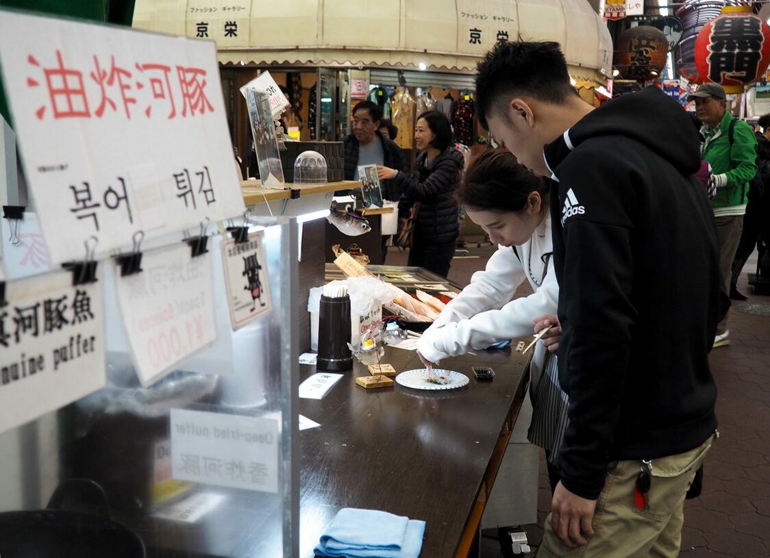 Una pareja china come tessa (sashimi de pez globo) en la entrada de Minami, restaurante especializado en pez globo del mercado Kuromon de Osaka (imagen del autor)