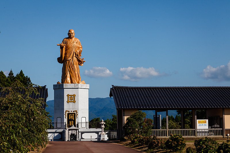 Estatua de bronce del monje Nichiren, dispuesta dando la espalda a la bahía de Ryōtsu. El monumento tiene 26 metros de altura, de los que 13 corresponden a la estatua y los otros 13 al pedestal.