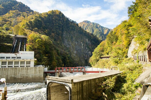 The 200-meter high cliff face of Nezumigaeshi looms beyond the red bridge at Kurobe Power Station No. 2.