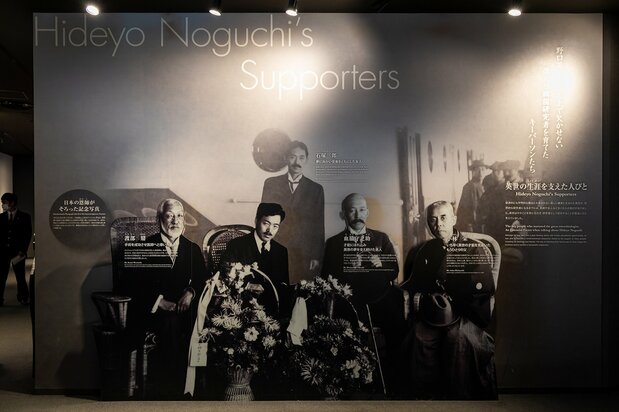 Noguchi assis en deuxième depuis la gauche, pose en 1915 avec les personnages clés de sa vie lors de son unique retour au Japon depuis son départ aux Etats-Unis en 1900. Depuis la gauche on retrouve : Watanabe Kanae, le premier docteur à avoir opéré la main brûlée de Noguchi ; Chiwaki Morinosuke, un dentiste qui fut le mentor et sponsor de Noguchi et Kobayashi Sakae, l’éducateur qui ouvrit la voie de l’éducation pour le jeune garçon d’Aizu. En arrière-plan on aperçoit Ishizuka Saburô, grand ami de Noguchi mais aussi son collègue à l’école dentaire de Takayama où Chiwaki lui offrit un travail.