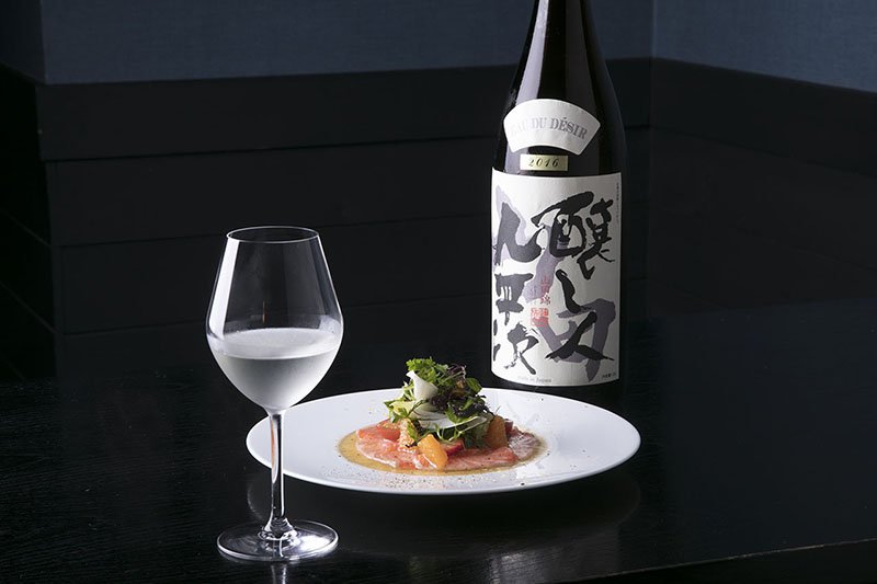 Maridaje de carpaccio de salmón con mézclum, cítrico y fresa, y Kamoshibito Kuheiji EAU DU DESIR Junmai Daiginjō Yamada Nishiki 2016, un sake elaborado con arroz de la marca Yamada Nishiki. Eau du desir significa ‘agua del deseo’ en francés.