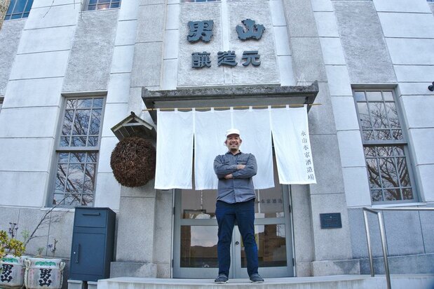 Nagayama Takahiro devant sa brasserie. À gauche du rideau noren se trouve un sugitama, une boule de branches de cèdre traditionnellement accrochée à l'entrée d'une brasserie de saké pour marquer la production d'un nouveau lot issu de la récolte de riz de l'année.