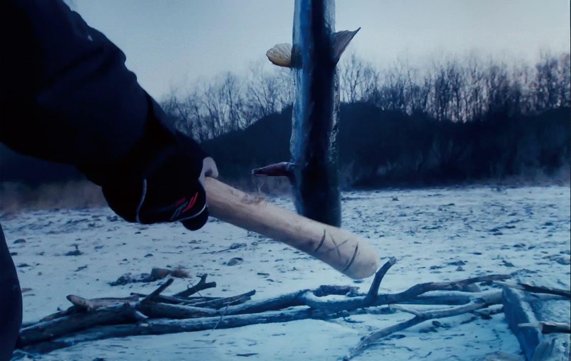 Shige golpea la cabeza del salmón con un ipakikni para matarlo. (© 2024 Takeshi Fukunaga/AINU PURI Production Committee)