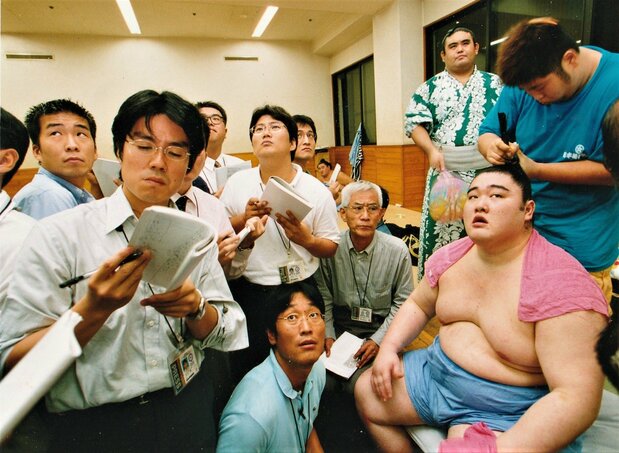 The shitaku beya are equipped with television monitors relaying the NHK live broadcasts. Back in the dressing room after his match, ōzeki Dejima (now oyakata, stable master, Ōnaruto) watches the action with reporters including the author, at front row center. (© Nagayama Satoshi)