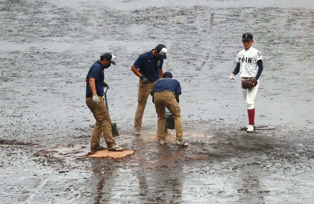 A sudden squall brings out Hanshin Engei workers as a player watches on August 17, 2021. (© Jiji)