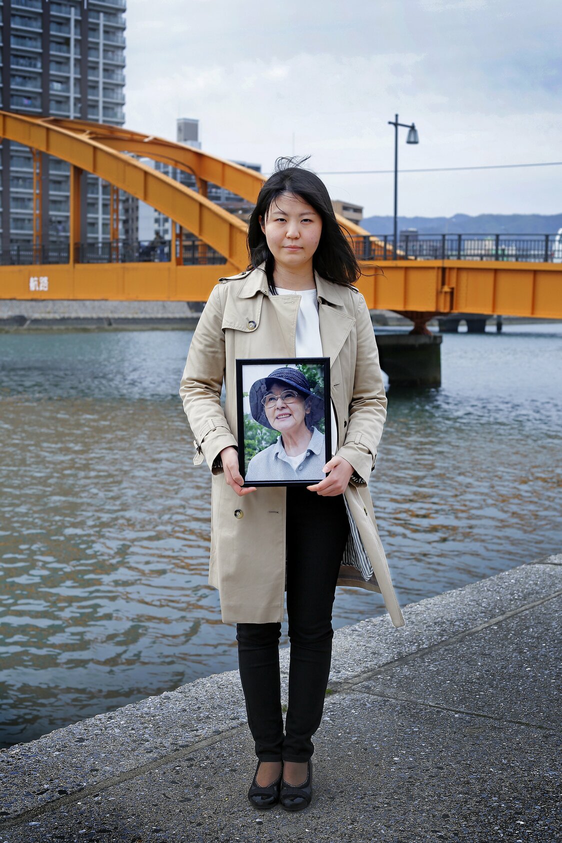住吉橋（広島市中区、爆心地から1.4キロ）で、祖母の遺影とともに立つ孫＝2019年3月。当時16歳の祖母は動員先の工場で被爆。家族を探しに市中心部に向かう際、この橋で川を流れる多くの死体を目撃したことを後に手記に残した。