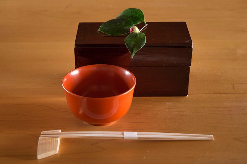 Cuenco y bentō de dos pisos, ambos lacados. La camelia de adorno, una wabisuke tsubaki, es una bella muestra del buen trato a los clientes.