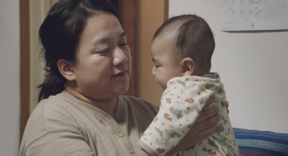 Yoshiki, el hijo menor, en brazos de Aika. Al final de la película ya camina. (© 2024 Takeshi Fukunaga/AINU PURI Production Committee)