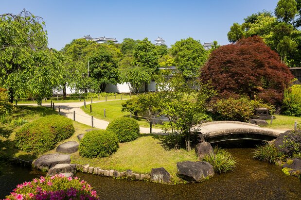 The top of the main donjon and the towers of the west bailey peek above the foliage of Kōkoen’s Flatly Landscaped Garden.