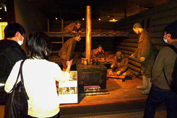 Young visitors to the Memorial Museum for Soldiers, Detainees in Siberia, and Postwar Repatriates gather around a diorama recreating a scene inside a Siberian labor camp. (© Saitō Katsuhisa)
