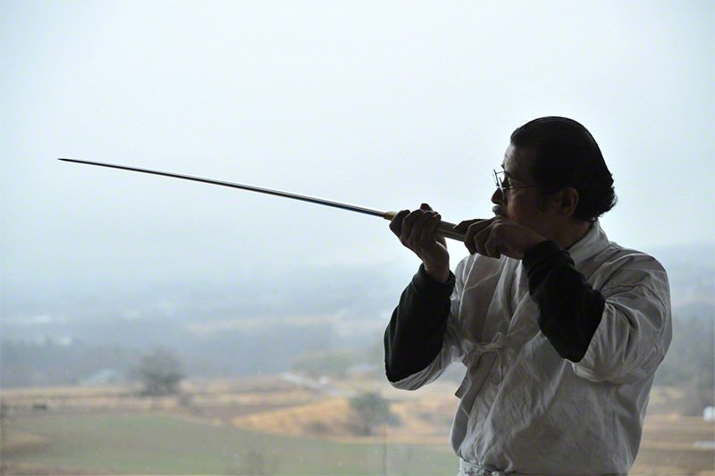 Le maître Miyairi observe minutieusement son katana achevé à la lumière, en le retournant, sous tous ses angles, de sa largeur à la forme de la pointe, en passant par le grain du métal et les motifs apparus sur la lame.