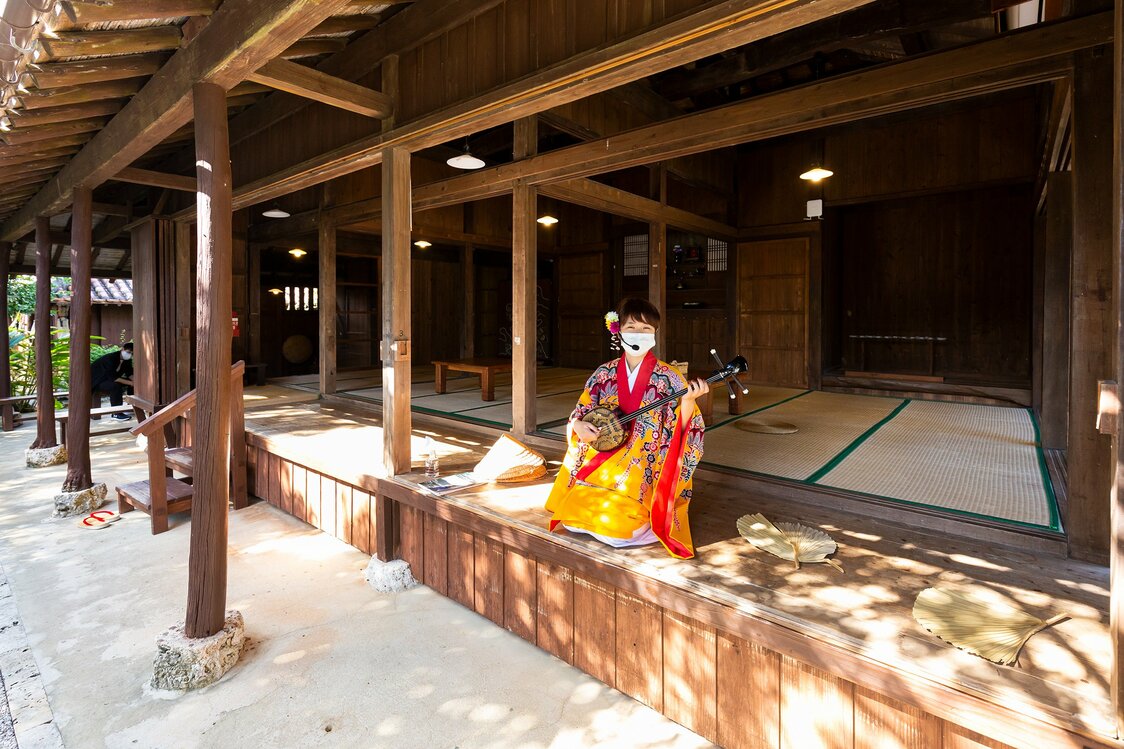 A performer plays a sanshin, a traditional Okinawan three-string instrument similar to a shamisen. Visitors are welcome to give it a try.
