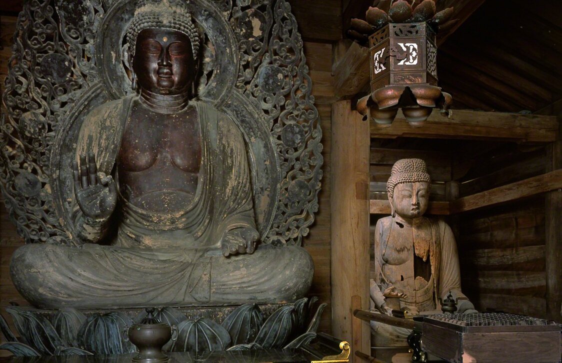 Two seated sculptures of Amida: the main image (on the left) with the damaged “old image” in the background. (© Muda Tomohiro)