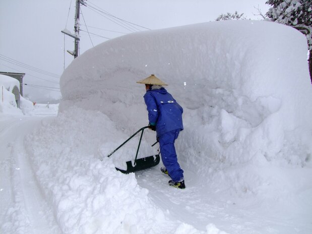 A person clears a path through a mountain of snow. (© Pixta)