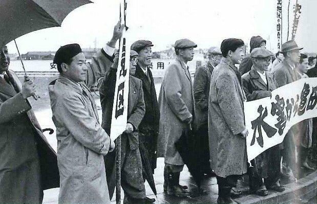 1959年4月、亀田郷土地改良区の役員は新潟市を訪問した首相岸信介を雨の降る新潟駅前でのぼり旗を掲げて出迎え、地盤沈下の被害を訴えた。左から2人目が佐野 提供:亀田郷土地改良区