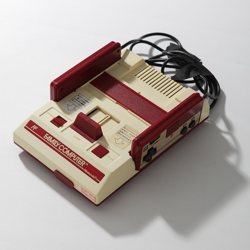 「ファミリーコンピュータ（ファミコン）」 （任天堂、1983年） 8ビットCPUを搭載し、ゲーム機本体のスロットに差し込むロムカセットを交換することによって多様なゲームを楽しくことを可能した家庭用据置型ゲーム機。