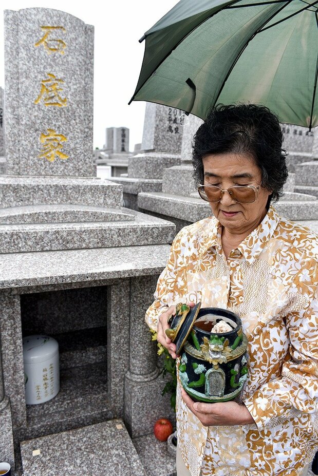 三女具志堅美智惠在石底加彌墓前抱著骨灰罈,照片裡可以看見罈中石頭,2019年5月28日,沖繩縣糸滿市(筆者攝影)