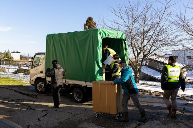 Déchargement d'un camion derrière l'école. Devant nous, des maisons effondrées.