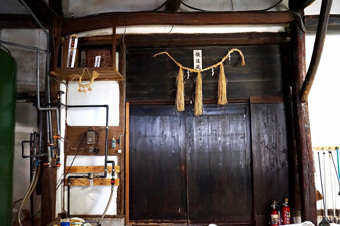 En la entrada de la bodega se cuelga una shimenawa, cuerdas trenzadas que se utilizan para proteger los sitios sagrados en el sintoísmo, hecha por el anterior tōji. Los grandes maestros de la generación que precedió a Imada tenían conocimientos que no se limitaban a la fabricación de sake. (Fotografía: Ukita Yasuyuki)