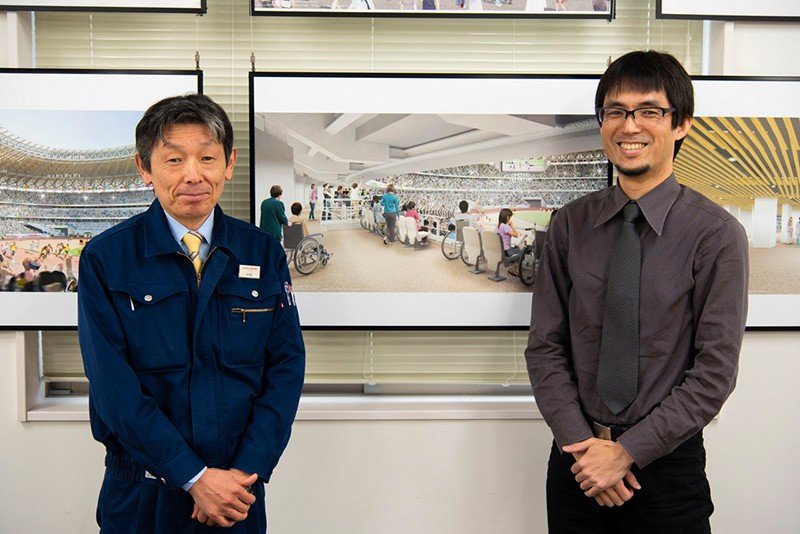 Komatsu Yukio (izquierda) y Tasaka Akihiko posan ante una fotografía que muestra cómo quedará una de las zonas del graderío del estadio reservada a las personas que usan sillas de ruedas y sus acompañantes.