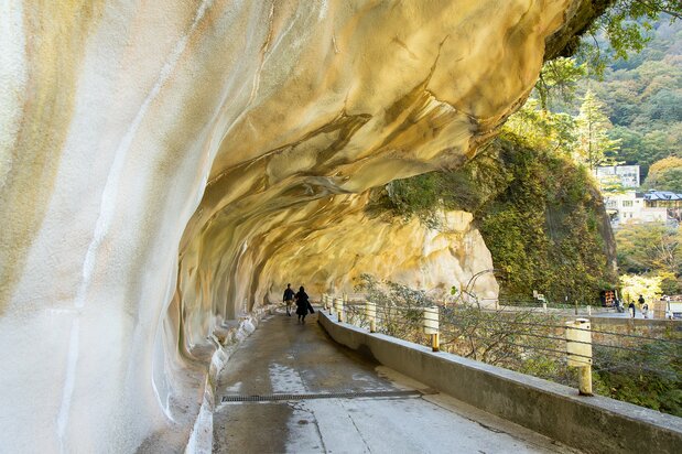 Visitors on the trail walk under a huge rock overhang.