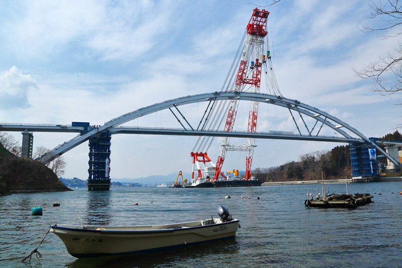 A massive crane barge sets the span down on its pillars. The main structure was built in Okayama Prefecture and shipped to Miyagi for installation.
