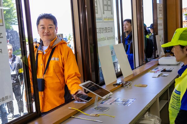 Le gouverneur de la préfecture de Yamanashi teste lui-même la barrière. Son bracelet muni d'un QR code qui est la preuve que le péage a été préalablement réglé en ligne.