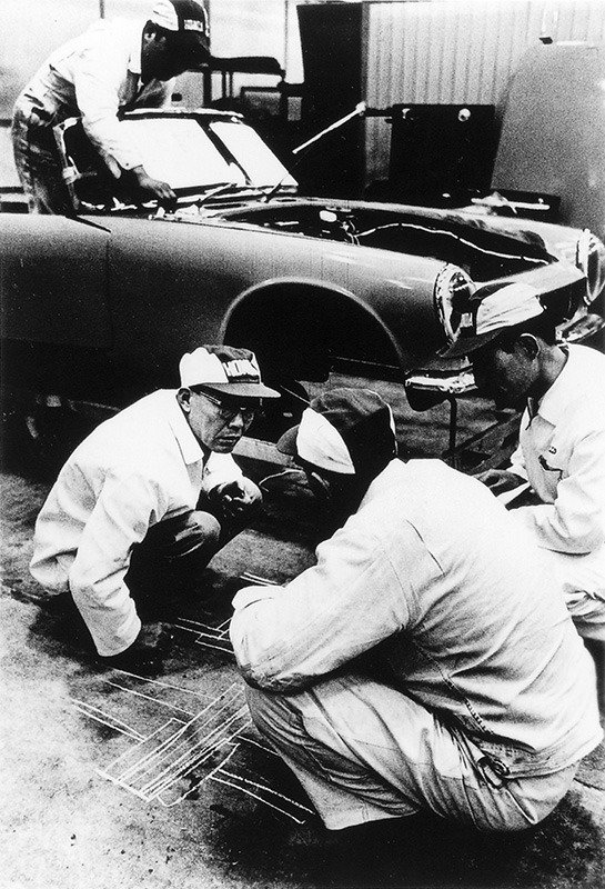 In a 1962 photo taken at the Wakō R&D center, Honda, left, writes diagrams on the floor to explain his ideas to engineers during the development of the S-series sports car.