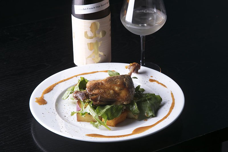 Muslo de pato confitado con salteado de calabaza, boniato, rábano y coles de Bruselas. Acompañamos este plato de carne sabroso y aromático con el Yamamoto Junmai Ginjō montrachet French Oak Barrel Aged.