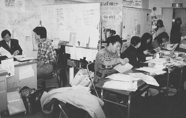田村太郎(左起第二位)開設的「外國人地震資訊中心」。1995年,當時手機與網路尚未普及,他們透過傳單、報紙、廣播來宣傳諮詢熱線的電話號碼(多元共融研究所提供)