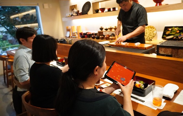 Comensales disfrutan de los platos servidos en cajas apiladas diseñadas por Taya Takahiro. (© Nakahara Mieko)