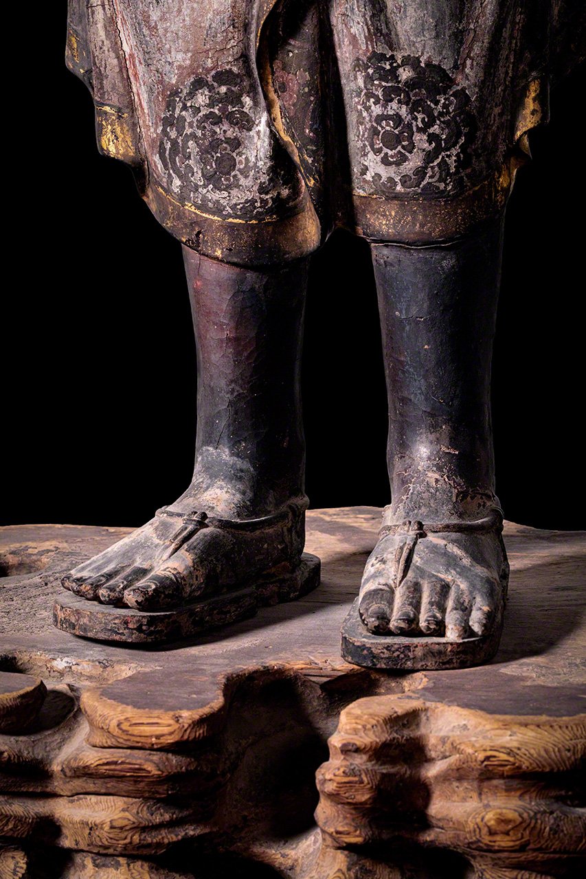 Calza sandalias con correas, algo que no se ve en muchas estatuas budistas, y que contribuye a darle un toque todavía más humano.